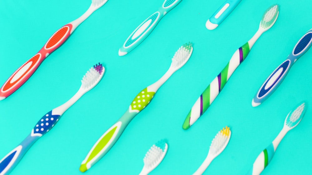 several toothbrushes with multicolored handles and bristles floating on a light blue, solid-colored background