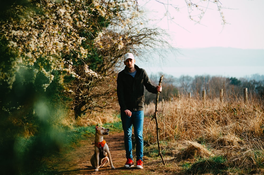 man in black jacket standing beside brown short coated dog during daytime