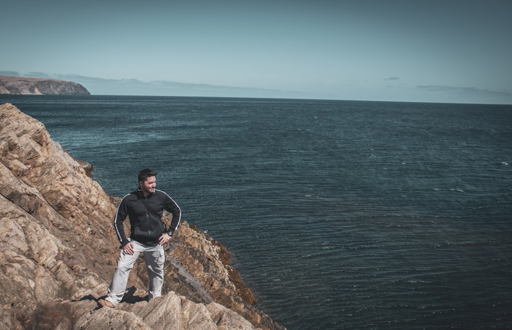 man in black t-shirt and gray shorts sitting on brown rock formation near body of near near near near