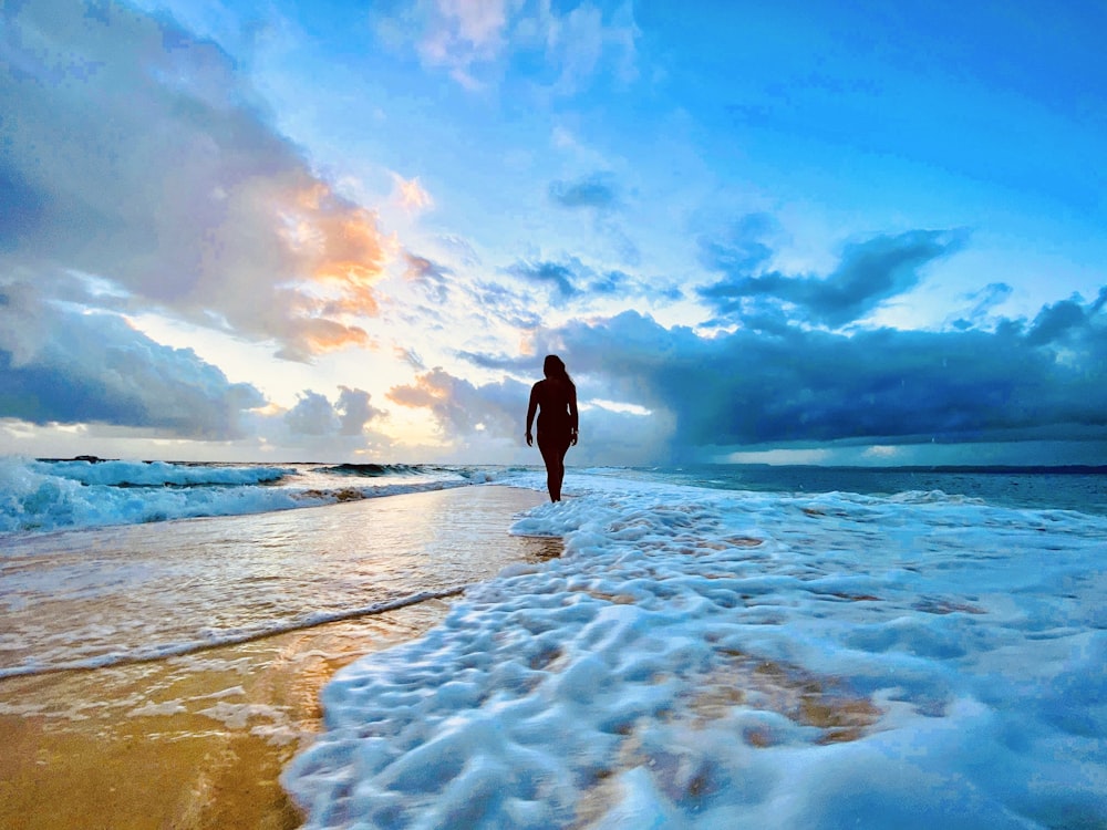 man in black jacket standing on seashore under blue and white cloudy sky during daytime