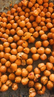 A close-up view of a pile of roasted chickpeas on a flat surface. The chickpeas are golden-brown in color and appear to be seasoned with various spices. They have a crispy texture and some are slightly broken.