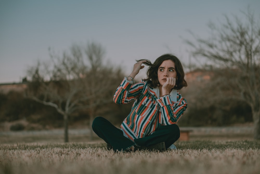 woman in red white and black striped long sleeve shirt sitting on grass field during daytime