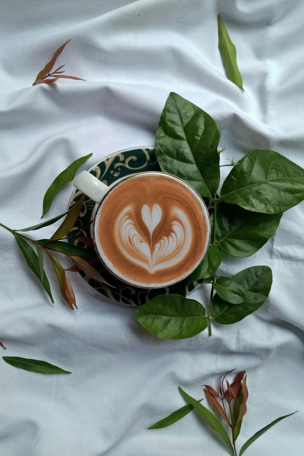 green and white ceramic cup with saucer on white textile