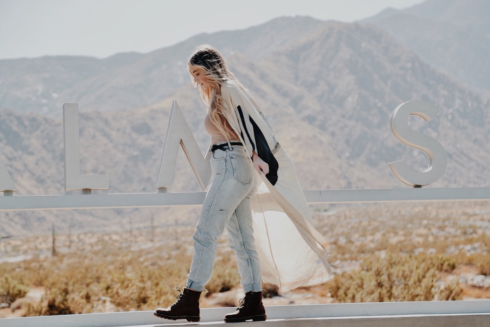 woman in white long sleeve shirt and blue denim jeans standing on brown field during daytime