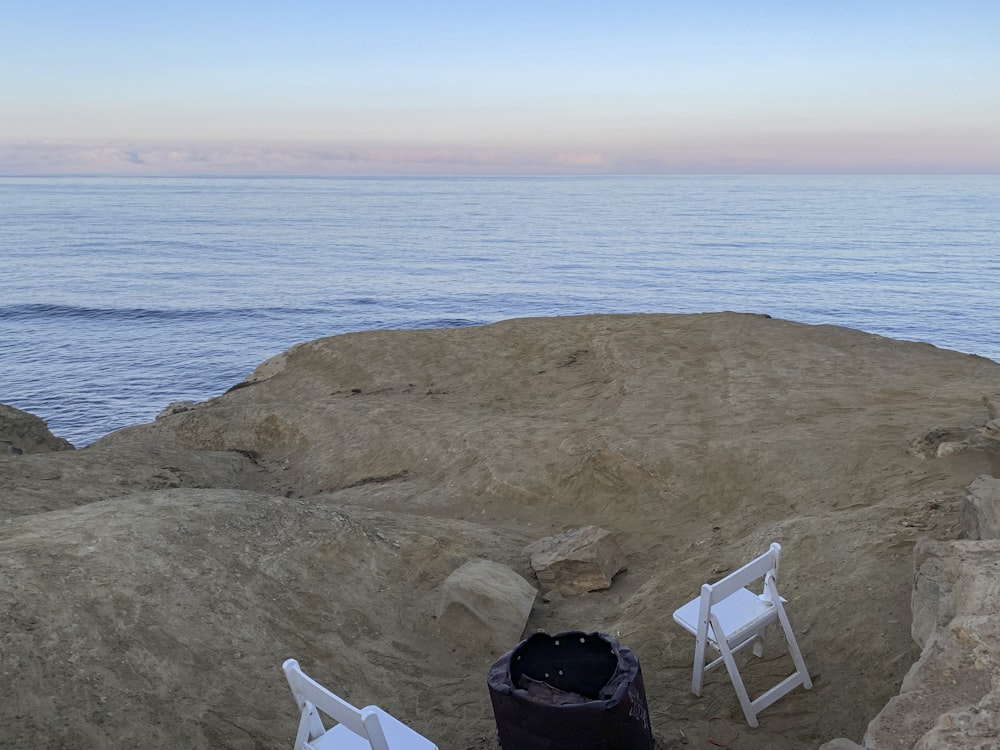 a couple of white chairs sitting on top of a rocky beach