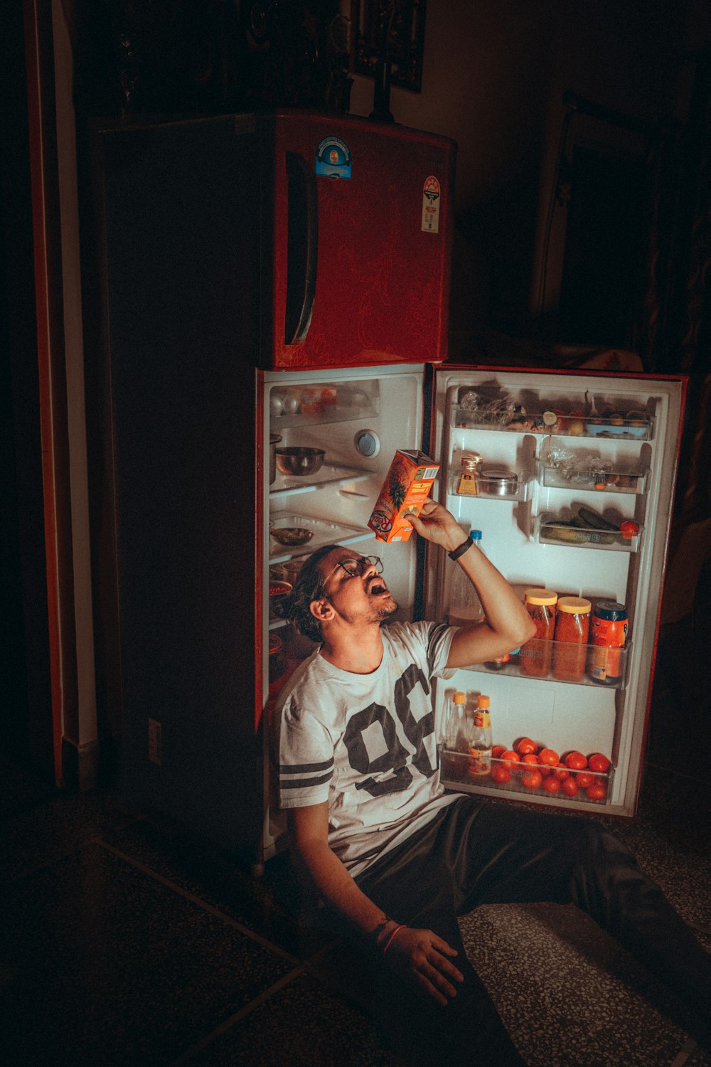 Chico en camiseta sin mangas blanca y negra de pie junto al refrigerador de montaje superior rojo