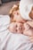 A mother lovingly embraces her baby on a soft white blanket. The baby is smiling and appears content and happy. The scene conveys a sense of warmth and tenderness.
