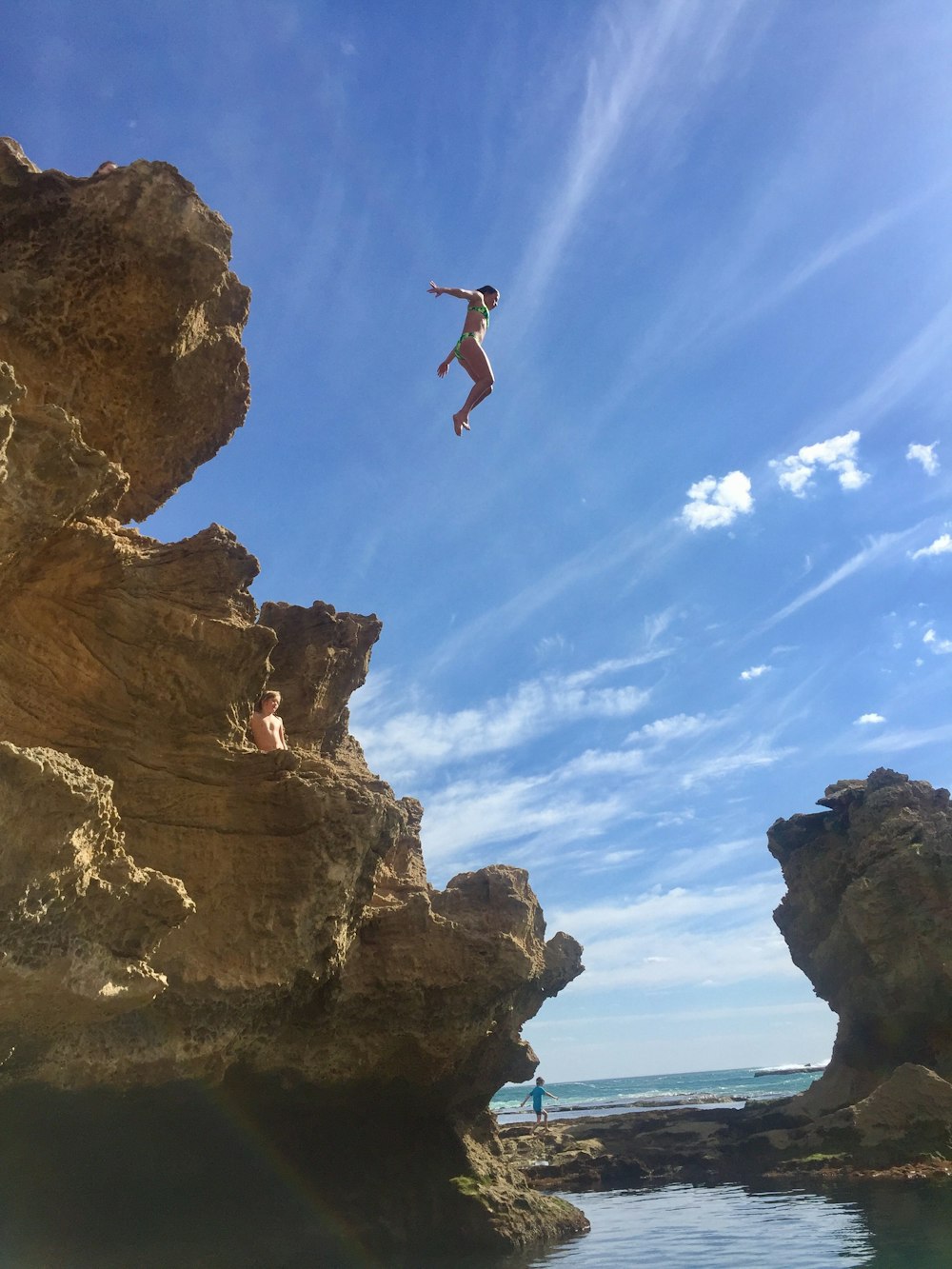 man jumping on brown rock formation during daytime
