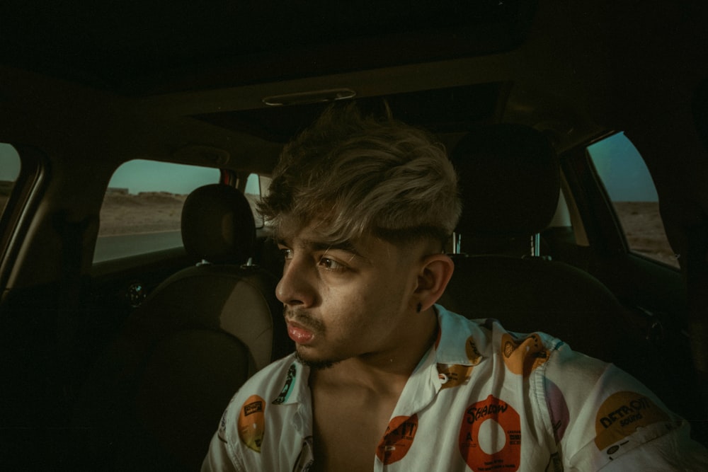 man in white and orange polo shirt sitting on car seat