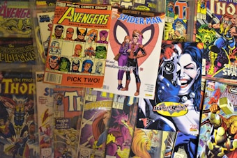 A collection of colorful comic book covers featuring popular characters such as the Avengers, Spider-Man, Thor, and Harley Quinn. The comics are arrayed in a slightly overlapping manner, displaying vibrant artwork and various superhero poses.