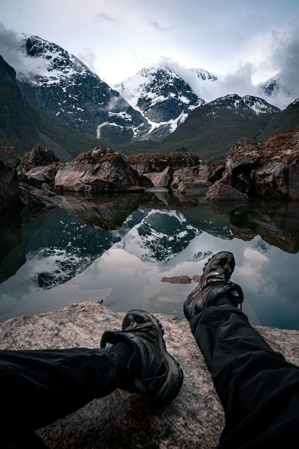 昼間、湖の近くの岩の上に座っている黒いズボンとハイキングシューズの人