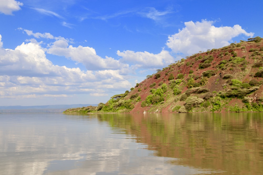 green and brown mountain beside body of water under blue sky and white clouds during daytime