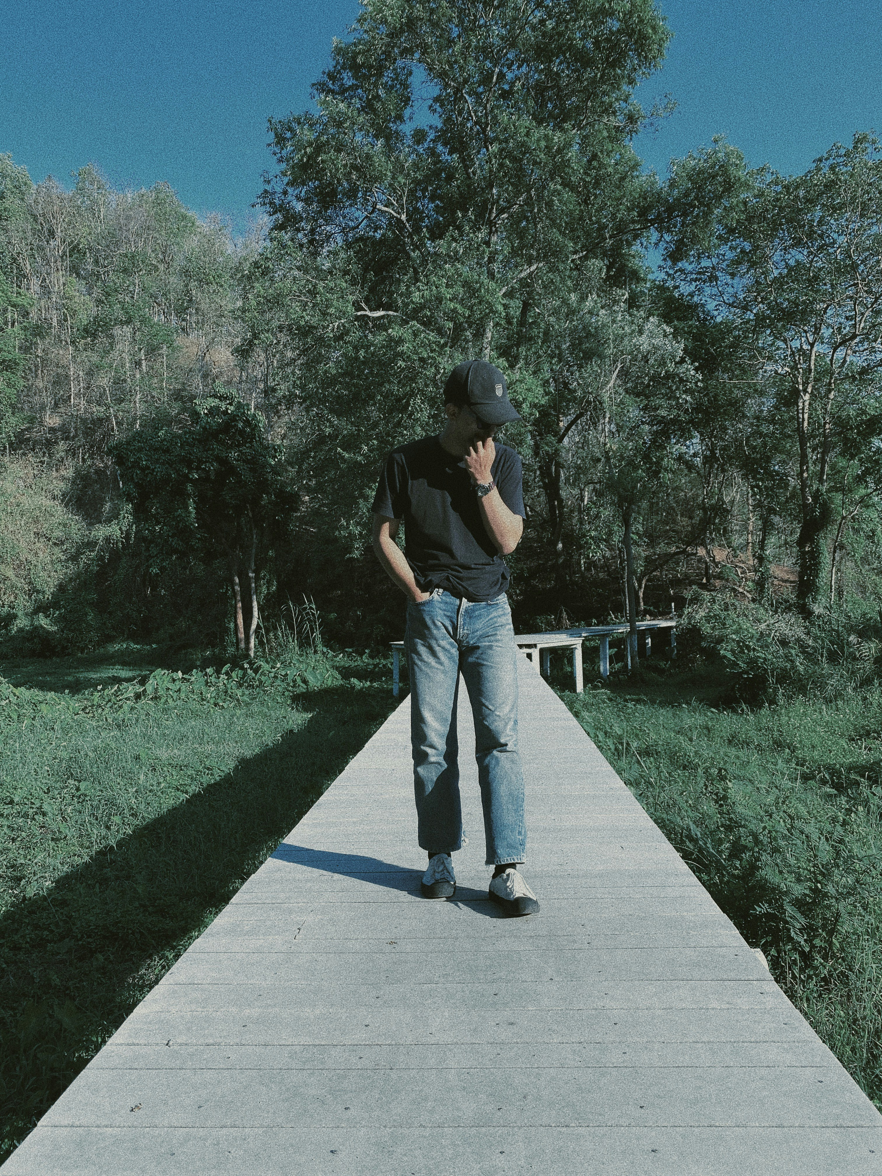 woman in black t-shirt and blue denim jeans standing on gray concrete pathway during daytime
