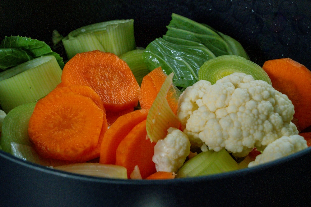 in Scheiben geschnittene Karotten und grünes Gemüse in schwarzer Schüssel
