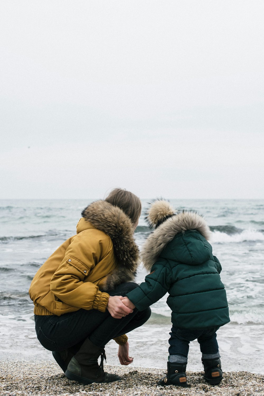 man and woman wearing parka jacket standing on beach during daytime
