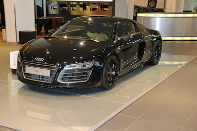 Shiny black sports car reflecting showroom lights, angled view.