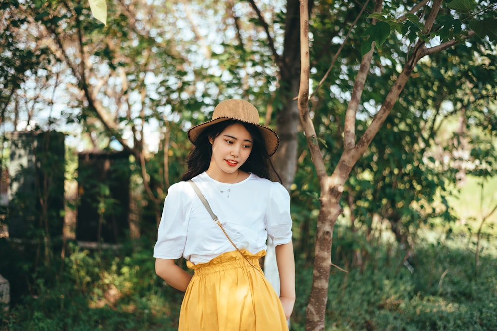 girl in white shirt and yellow skirt standing under green tree during daytime