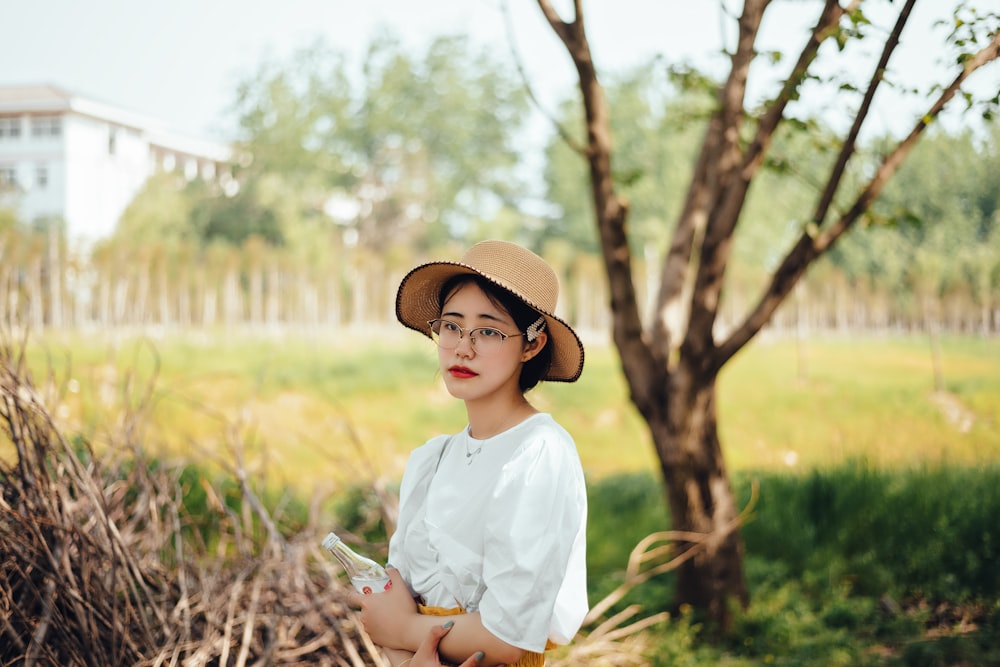 woman in white dress shirt and brown hat standing near green grass during daytime