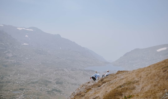 person in white shirt and black pants sitting on brown rock mountain during daytime in Kosciuszko National Park NSW Australia