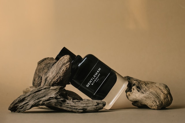 A bottle of men's fragrance labeled 'Gentleman Givenchy' is artfully positioned among pieces of driftwood, set against a warm beige background.