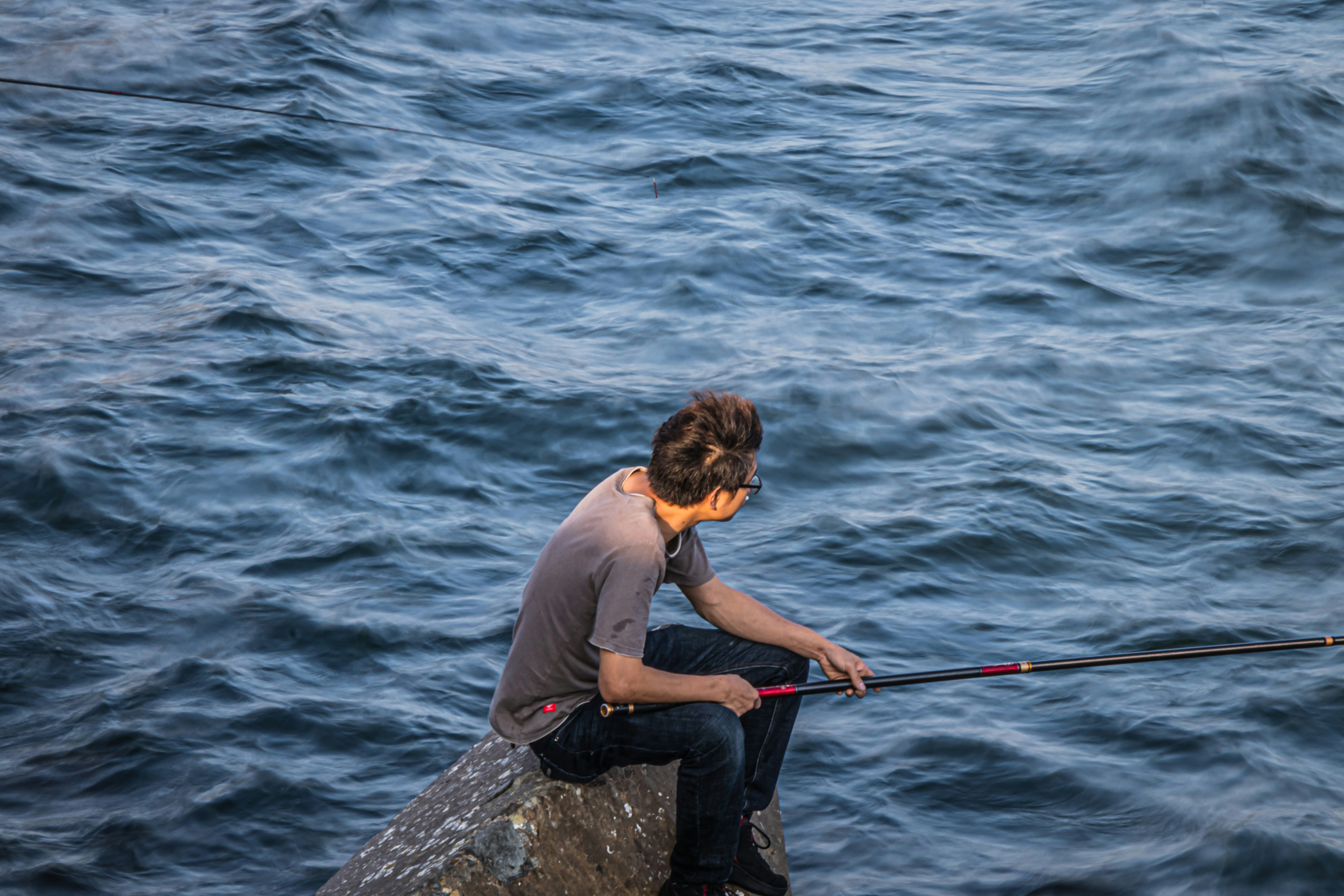 man in blue shirt and black pants sitting on rock in front of sea