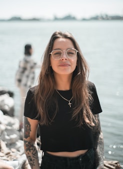 woman in black crew neck t-shirt wearing brown framed eyeglasses standing on rocky shore during