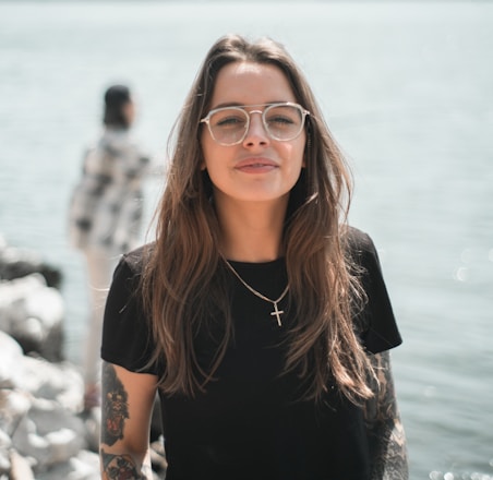 woman in black crew neck t-shirt wearing brown framed eyeglasses standing on rocky shore during