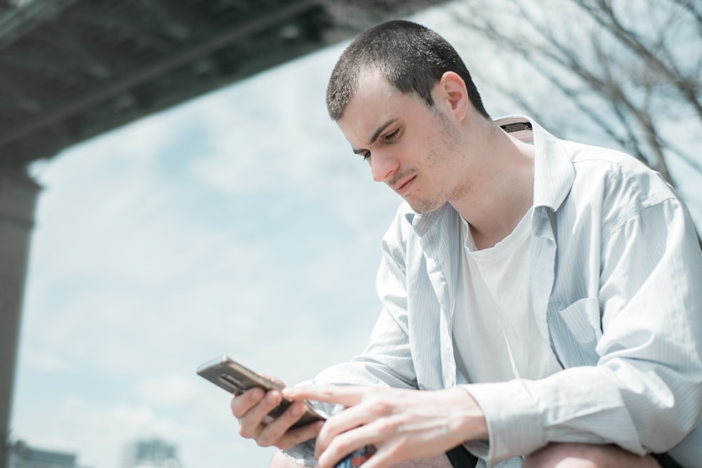 man in white dress shirt holding smartphone