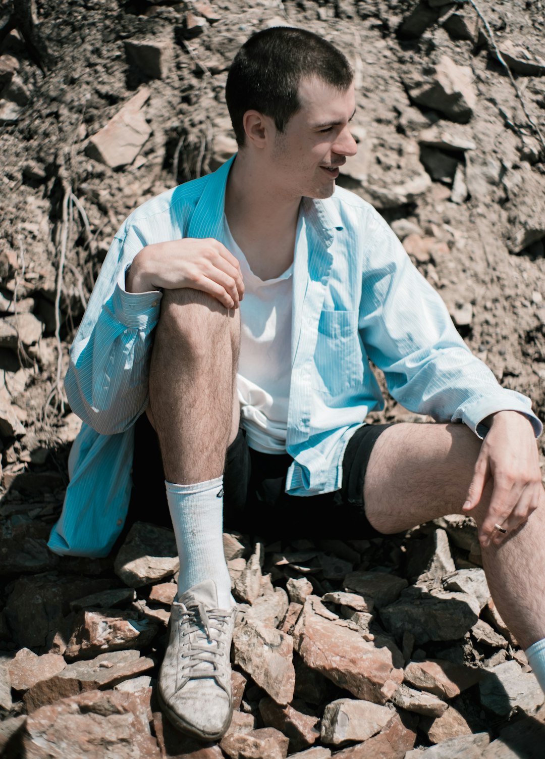 man in white dress shirt and black shorts sitting on rock during daytime