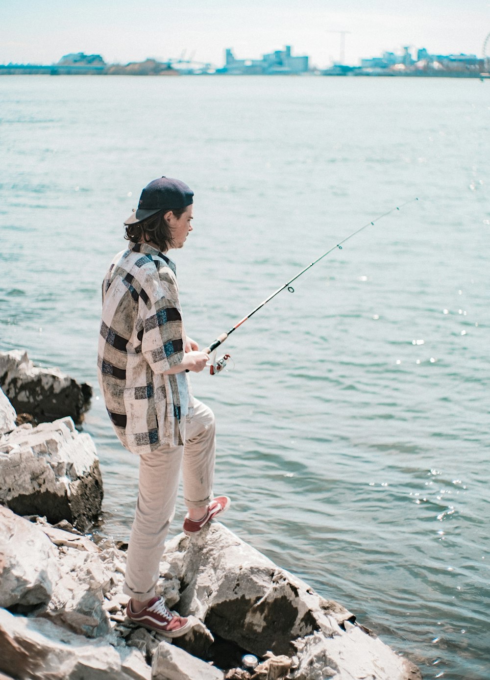 青と白の格子縞のドレスシャツと茶色のズボンを着た男が昼間に海で釣りをしている