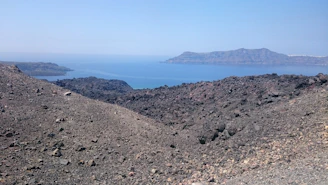 A panoramic view of Santiago Island's volcanic landscape meeting the turquoise Atlantic Ocean under a bright sky.