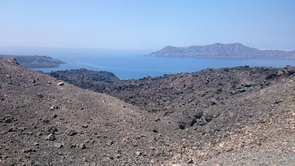A panoramic view of Santiago Island's volcanic landscape meeting the turquoise Atlantic Ocean under a bright sky.