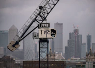Heavy machinery lifting steel beams into place with the Dallas skyline in the background.