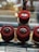 A display of three round red velvet cakes, each topped with glossy chocolate frosting, placed neatly on a reflective glass surface. The cakes are rich in texture and color, creating an inviting, luscious appearance. Below them, a label reads 'REDVELVET CHOCOLATE' in both English and Arabic.