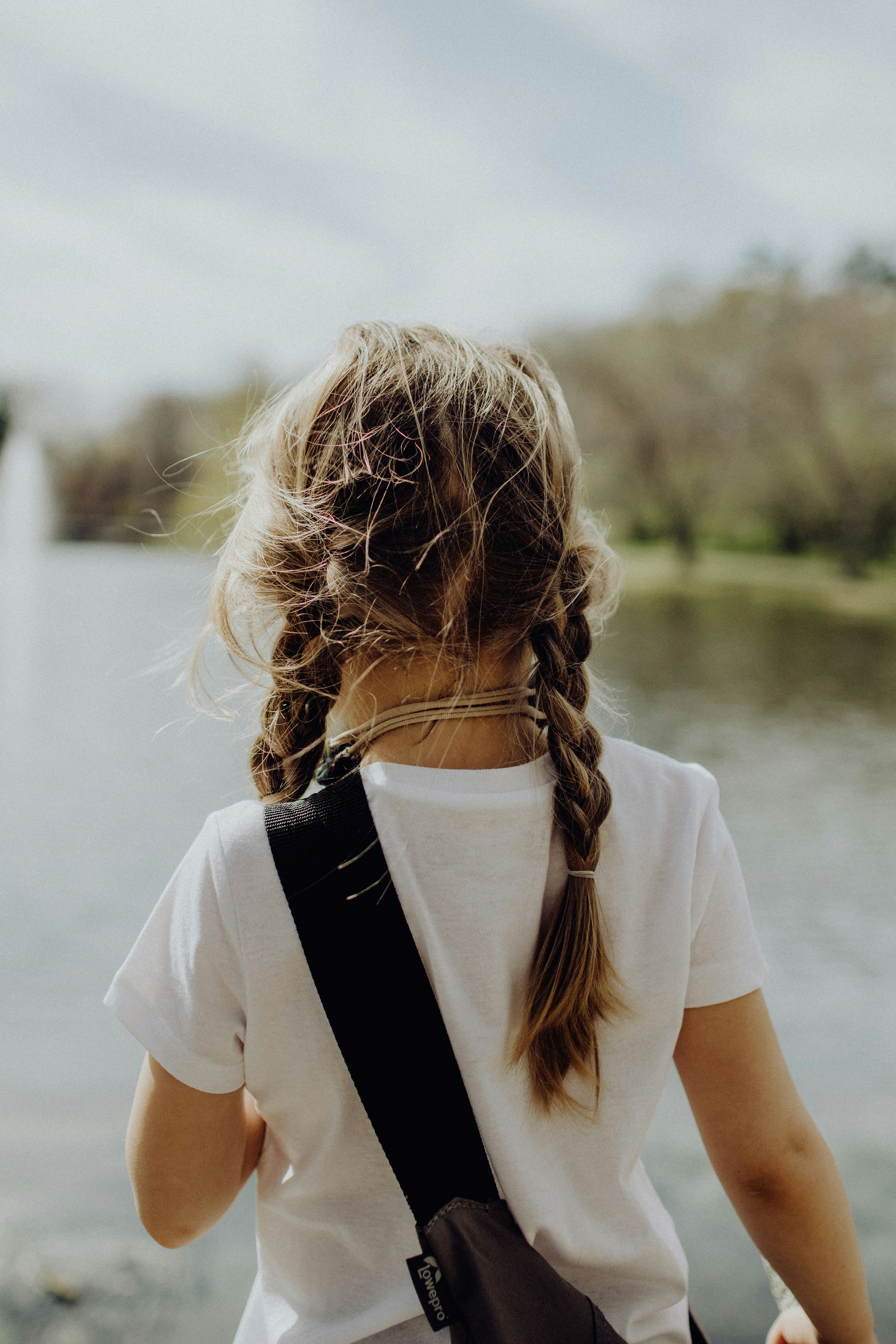 Little girl in a white T shirt with braids and a bag slung over her shoulder