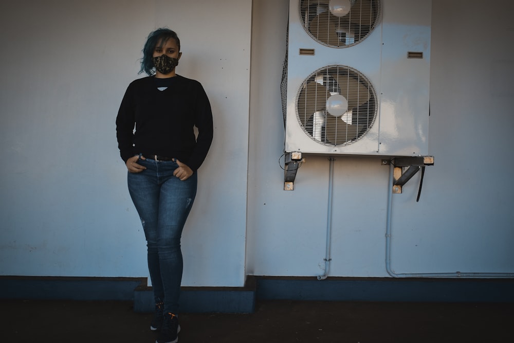 woman in black long sleeve shirt and blue denim jeans standing beside white wall