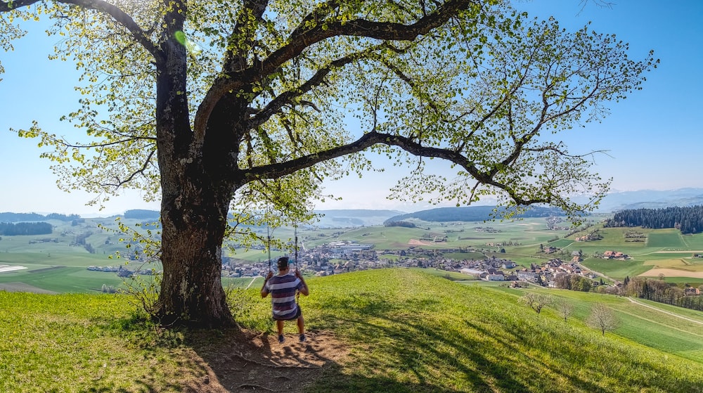 man in brown shirt and black shorts sitting on brown tree branch during daytime