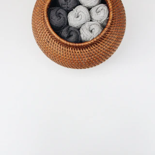 A small desktop basket filled with colorful yarn balls beside a cozy armchair.