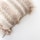 A close-up of a decorative pillow featuring intricate crochet patterns and tasselled fringes. The fabric showcases alternating rows of open stitches and densely woven textures, giving a handcrafted and artisanal appearance.