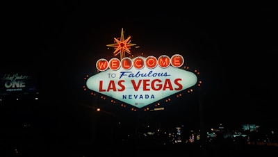 A bright and iconic sign illuminated at night, displaying a warm welcome to Las Vegas, Nevada. The sign is prominently lit with neon lights, featuring the phrase 'Welcome to Fabulous Las Vegas Nevada' with a star at the top.