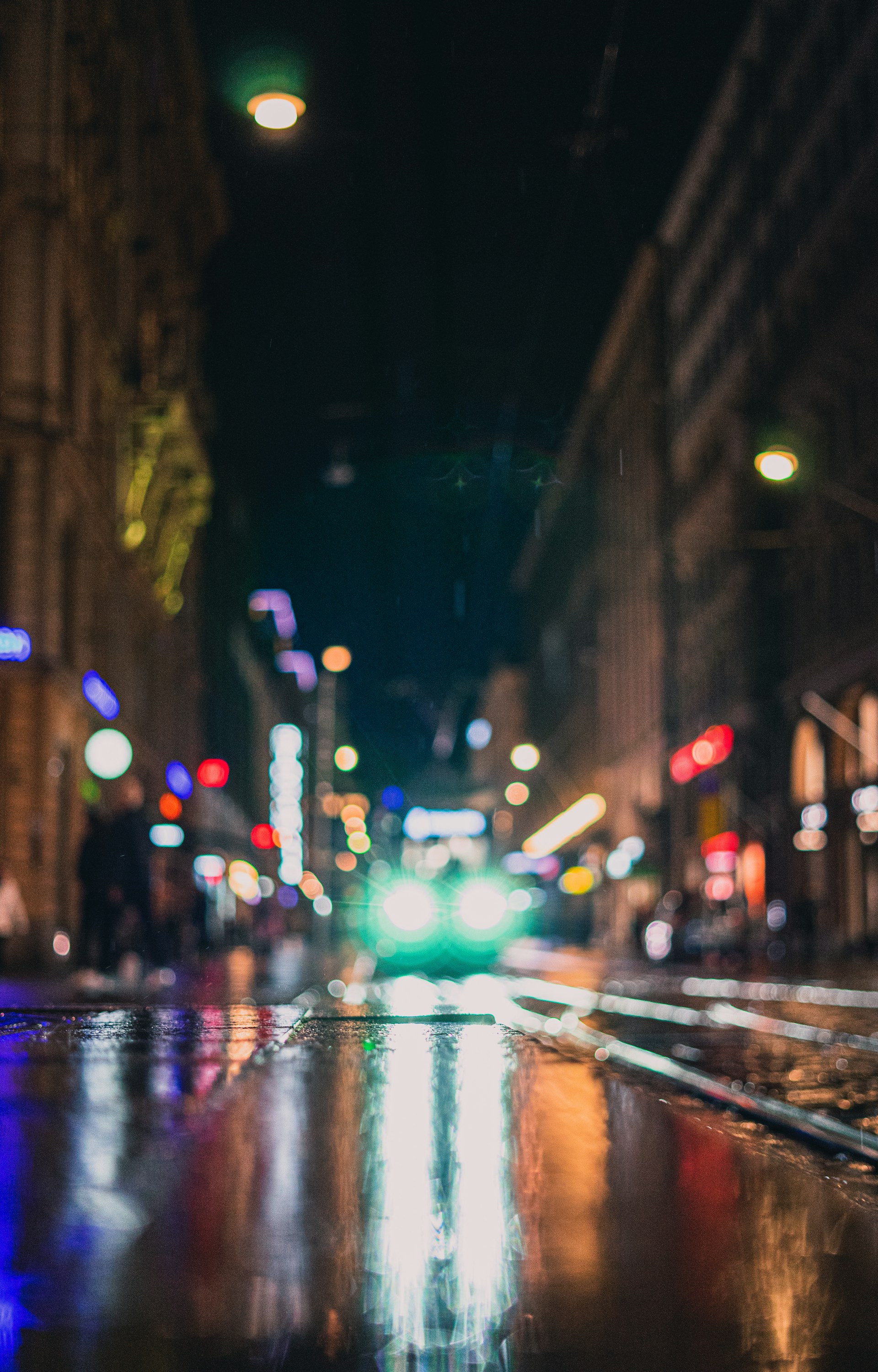 An urban street scene at dusk, with vibrant colors reflecting off wet pavement and blurred motion of passing pedestrians.