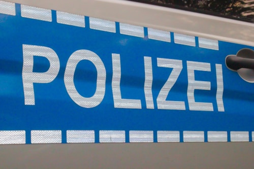 A section of a police vehicle displaying the word 'POLIZEI' in bold white letters on a blue background with reflective elements. The design includes a pattern of white squares along the top and bottom edges.