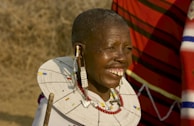 Close-up of a Maasai warrior adorned in traditional red shuka and beadwork, smiling warmly.