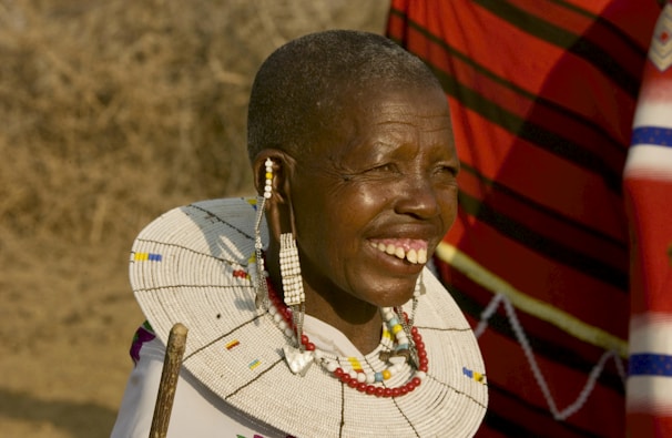 A close-up of a colorful Maasai warrior smiling against a backdrop of rolling hills.
