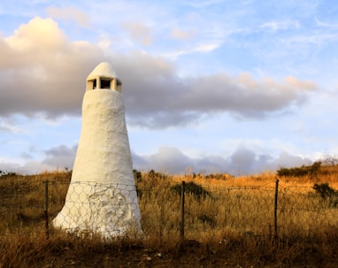 white concrete tower on brown grass field under white clouds