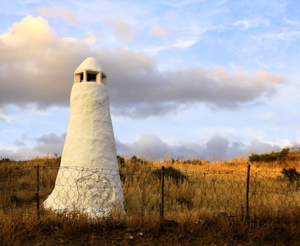 white concrete tower on brown grass field under white clouds