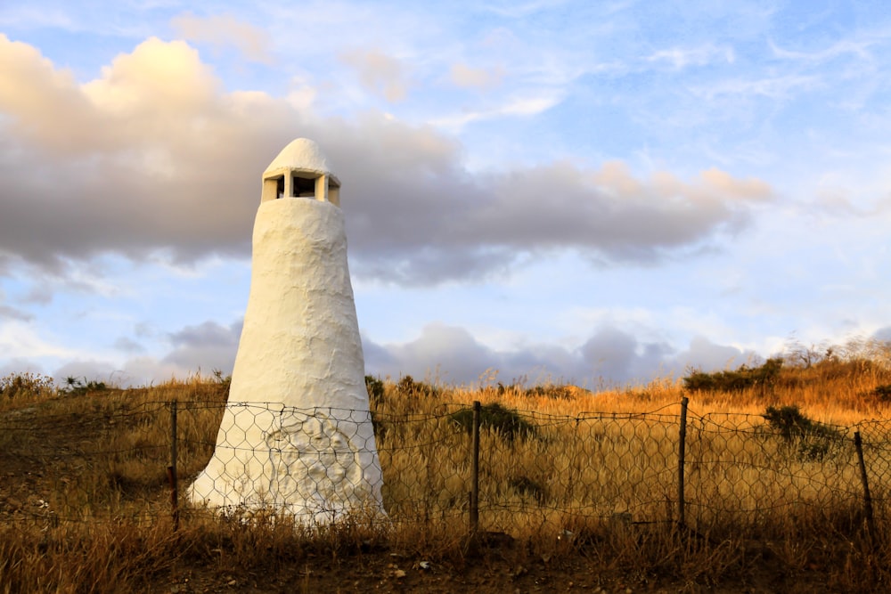 white concrete tower on brown grass field under white clouds