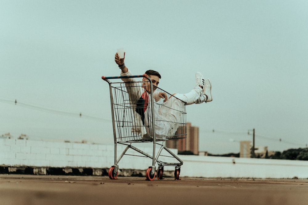 woman in white jacket and blue denim jeans riding on shopping cart during daytime