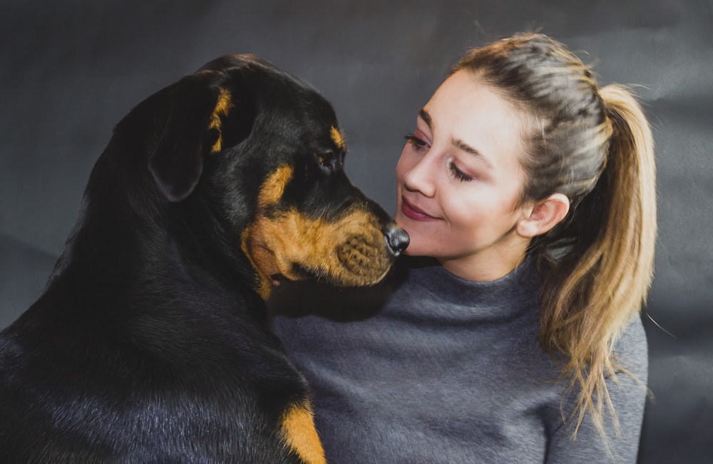 woman in black crew neck shirt hugging black and tan short coat dog