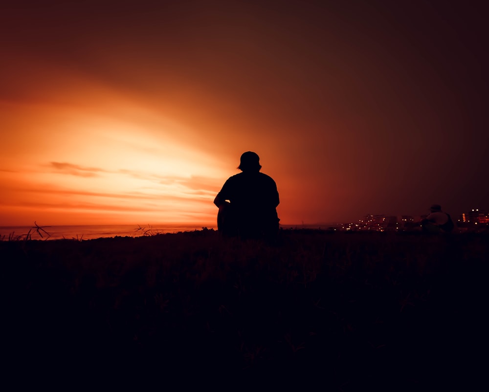 silhouette of man sitting on grass during sunset